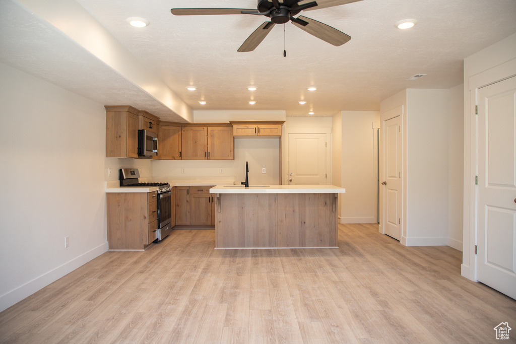 Kitchen featuring stainless steel appliances, light countertops, light wood finished floors, a center island, and a ceiling fan