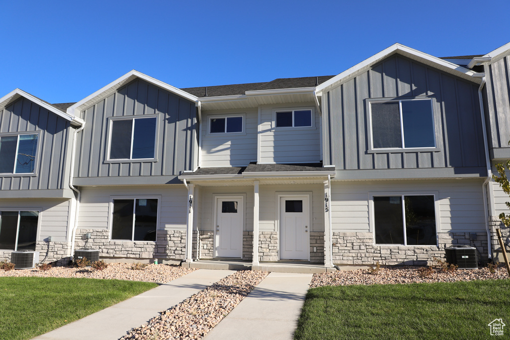 Townhome / multi-family property with a front lawn, board and batten siding, stone siding, and cooling unit