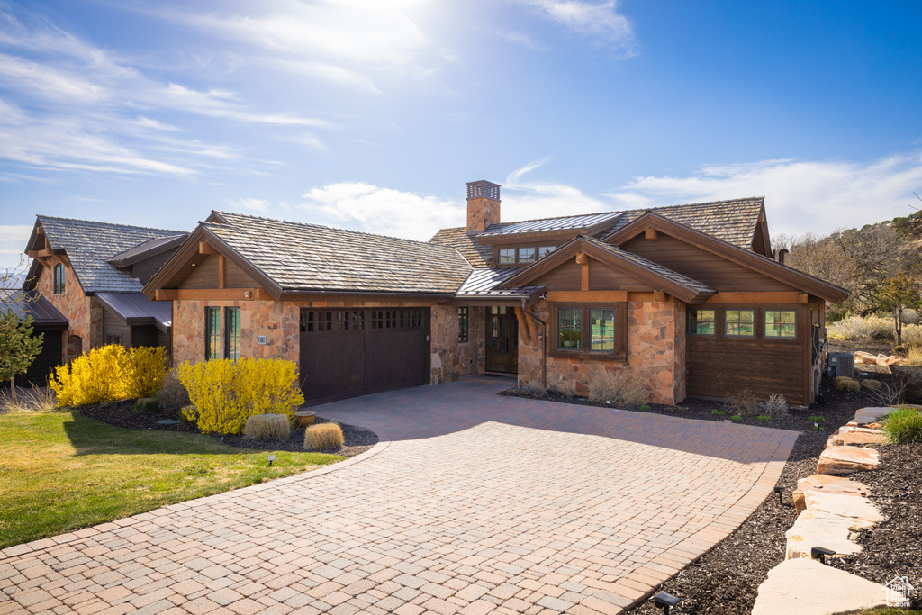 View of front of house with a garage, stone siding, decorative driveway, a chimney, and a standing seam roof