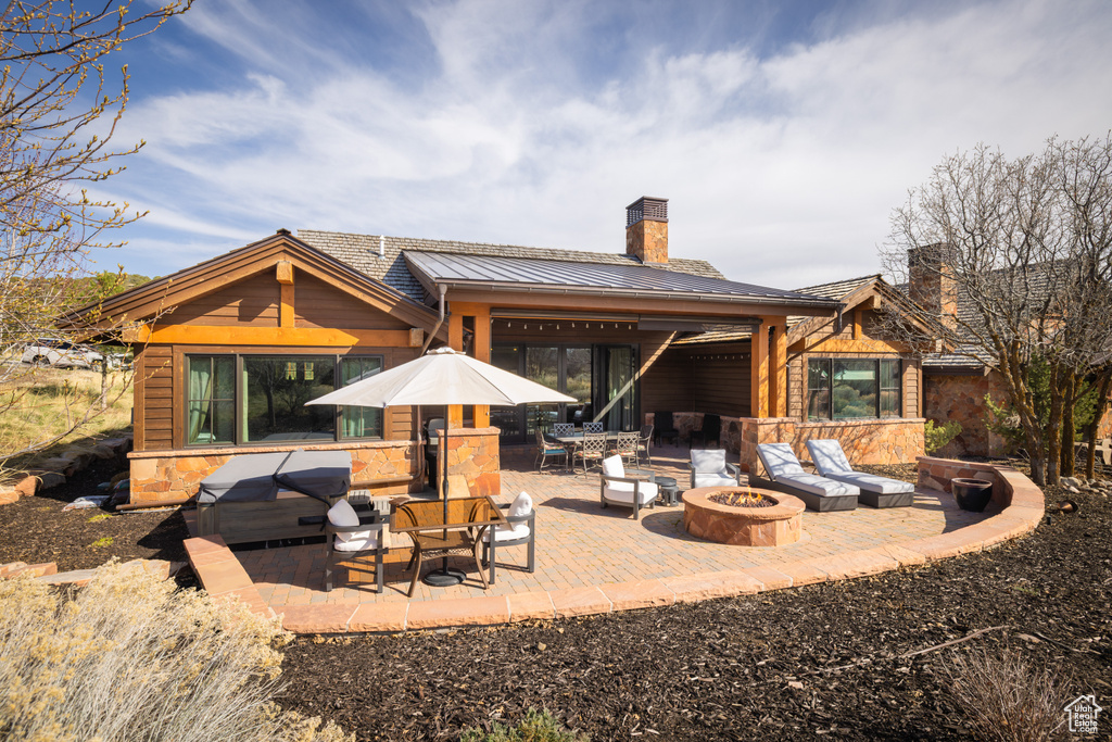 Back of house featuring an outdoor living space with a fire pit, a chimney, a standing seam roof, a patio, and metal roof