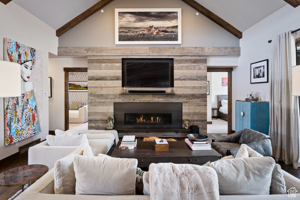 Living area with high vaulted ceiling, a lit fireplace, beam ceiling, and wood finished floors