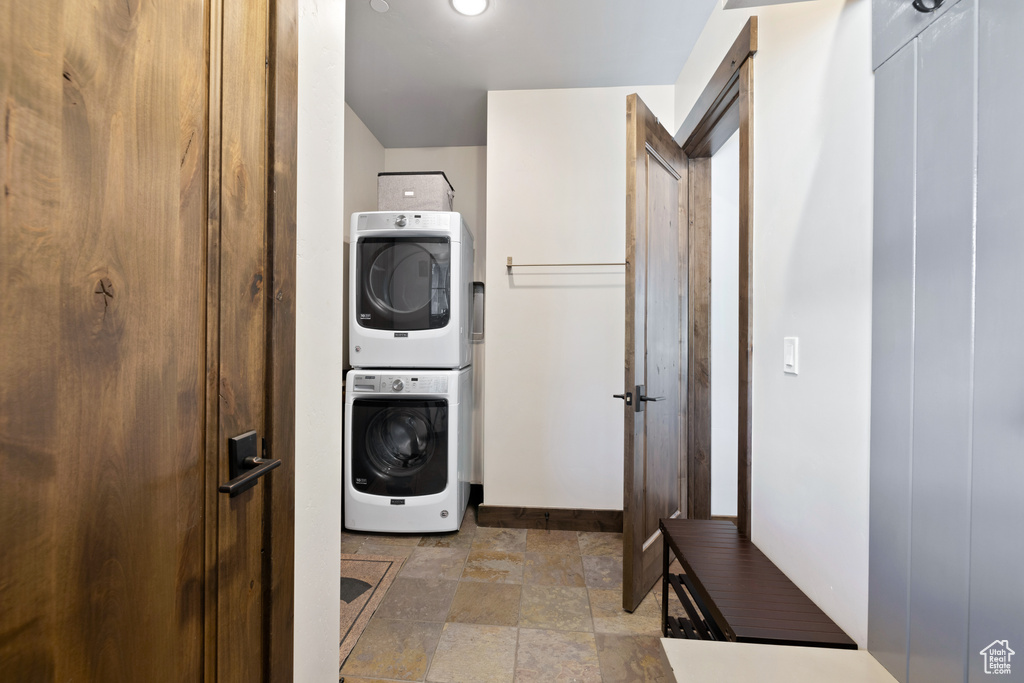 Laundry area featuring baseboards, stacked washer / drying machine, stone finish floor, and laundry area