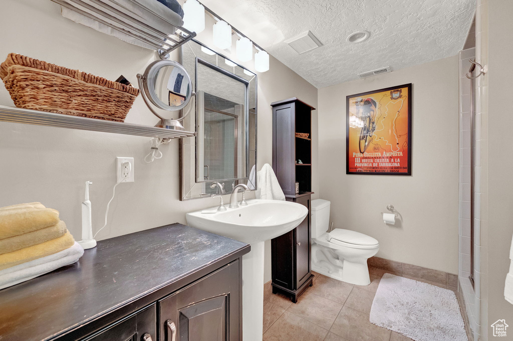 Full bath featuring tile patterned flooring, toilet, a textured ceiling, baseboards, and a shower stall