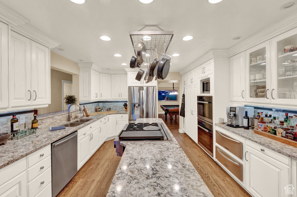 Kitchen featuring tasteful backsplash, light stone counters, white cabinets, a warming drawer, and stainless steel appliances