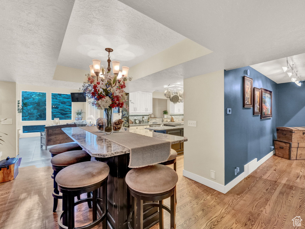Dining room with baseboards, a textured ceiling, an inviting chandelier, and light wood-style flooring