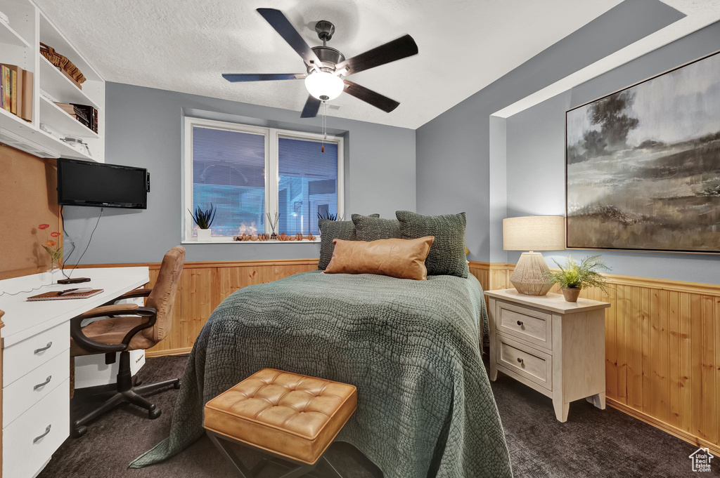 Bedroom featuring wooden walls, a ceiling fan, wainscoting, and dark colored carpet