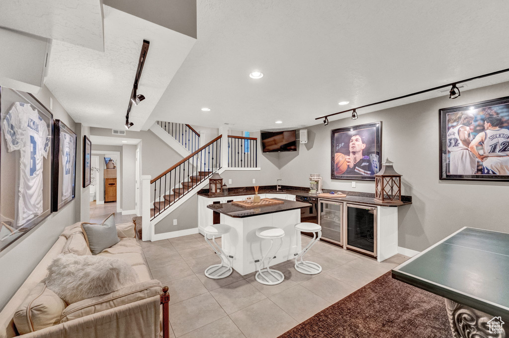Living area with light tile patterned floors, rail lighting, wet bar, and stairway