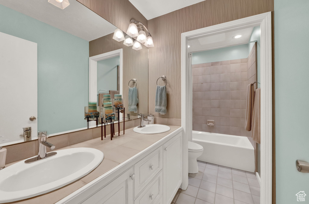 Bathroom with double vanity, a sink, tile patterned floors, and toilet