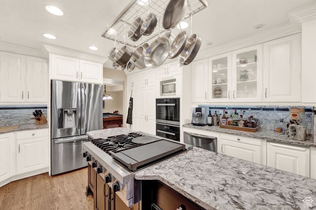 Kitchen featuring tasteful backsplash, light stone countertops, stainless steel appliances, and white cabinetry
