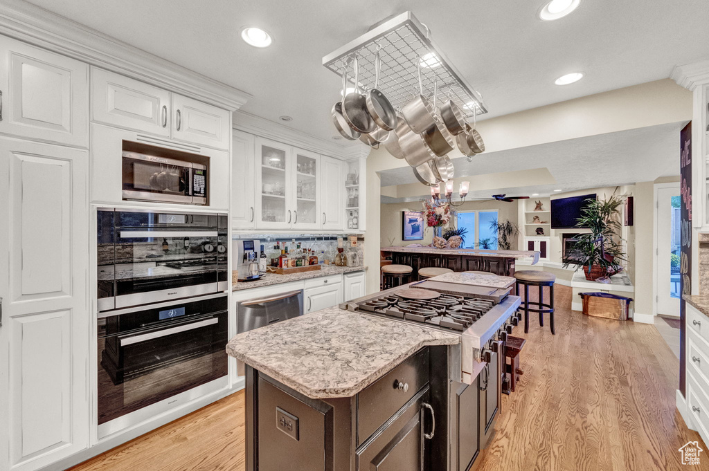 Kitchen with white cabinets, an inviting chandelier, stainless steel appliances, open floor plan, and recessed lighting