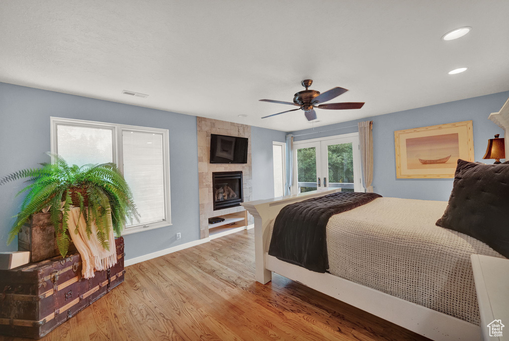 Bedroom featuring ceiling fan, french doors, visible vents, a large fireplace, and wood finished floors