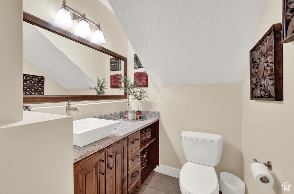 Bathroom with a textured ceiling, tile patterned flooring, vaulted ceiling, vanity, and toilet