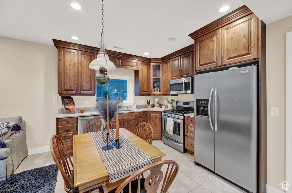 Kitchen featuring pendant lighting, appliances with stainless steel finishes, light tile patterned floors, light countertops, and glass insert cabinets