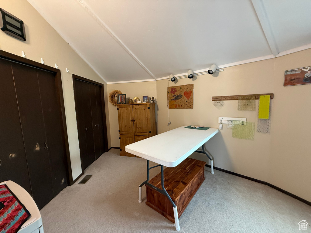 Office space featuring baseboards, visible vents, vaulted ceiling, and light colored carpet