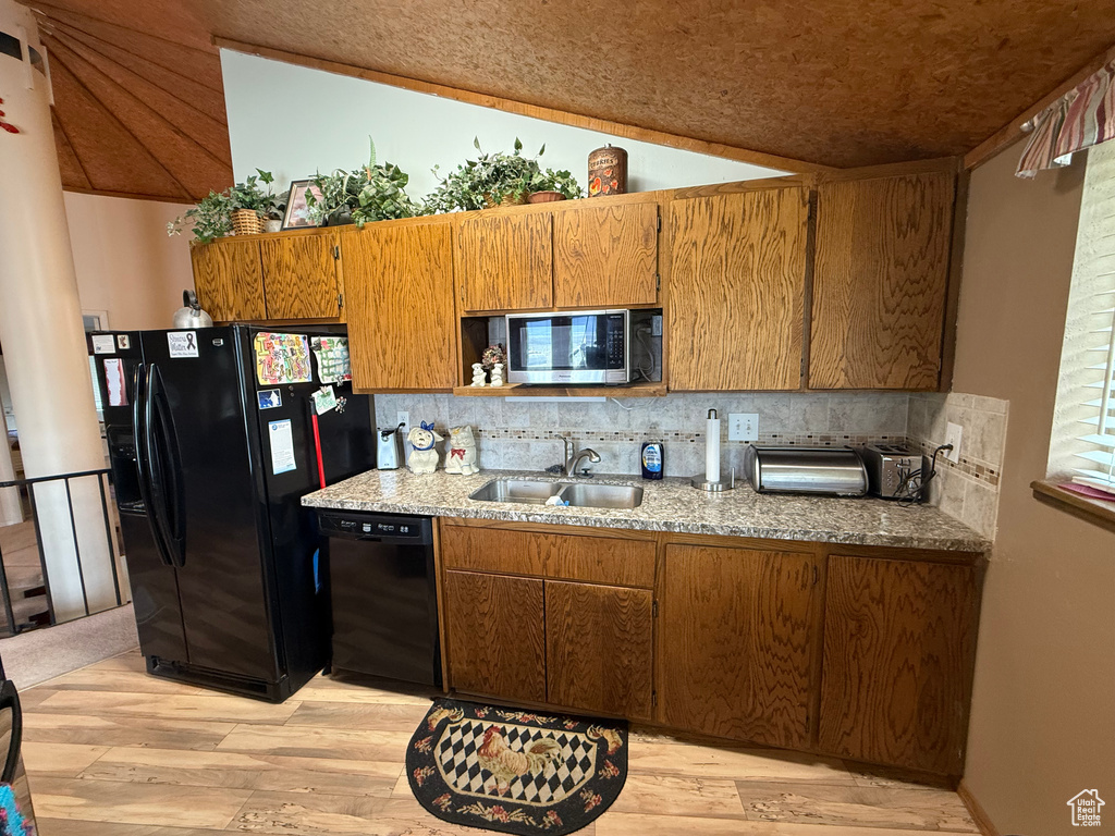 Kitchen with decorative backsplash, brown cabinets, a sink, light wood finished floors, and black appliances
