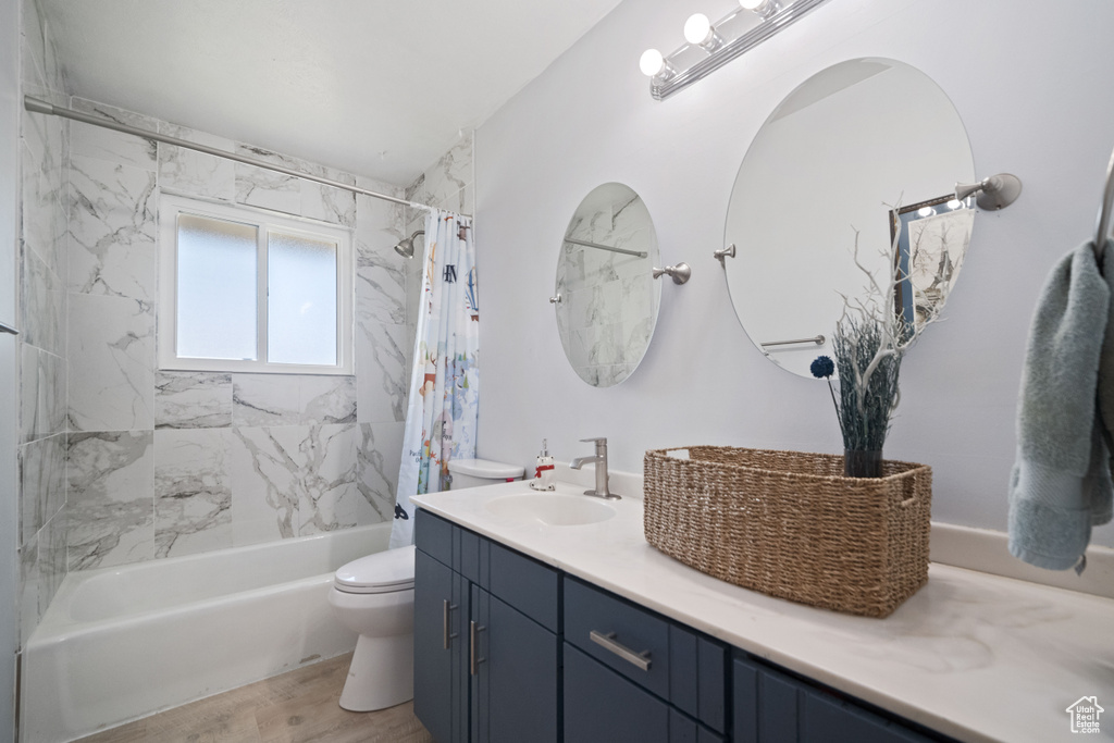 Full bath with vanity, shower / tub combo with curtain, wood finished floors, and toilet