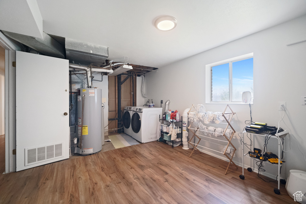 Basement with visible vents, gas water heater, light wood finished floors, and washing machine and clothes dryer