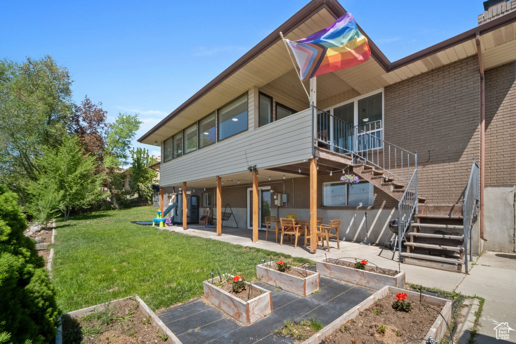 Back of house with stairs, brick siding, a vegetable garden, a patio area, and a yard