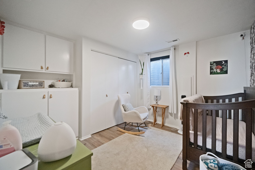 Bedroom with visible vents, a crib, light wood-style flooring, and a closet