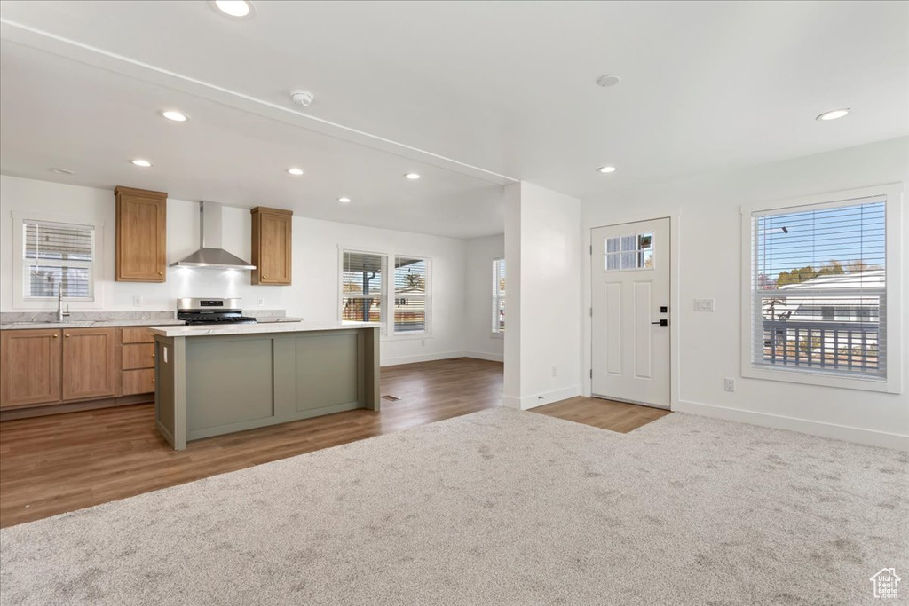 Kitchen featuring wall chimney range hood, stainless steel range, recessed lighting, baseboards, and a kitchen island