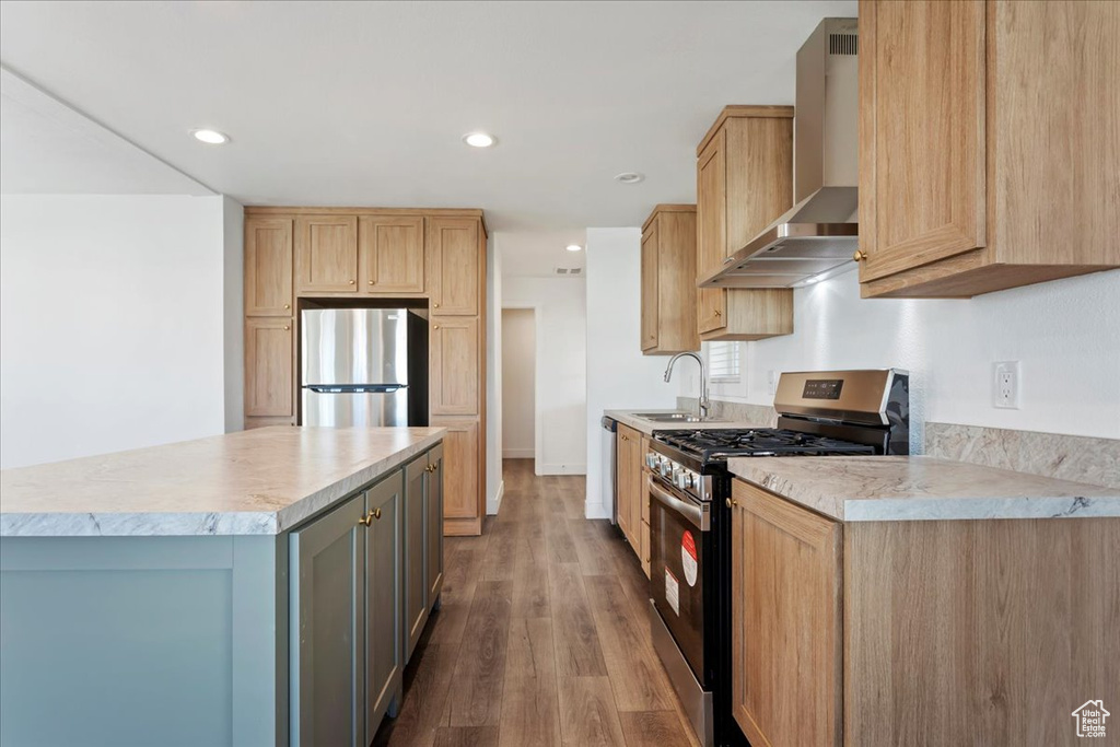 Kitchen with wall chimney range hood, appliances with stainless steel finishes, a sink, light countertops, and wood finished floors