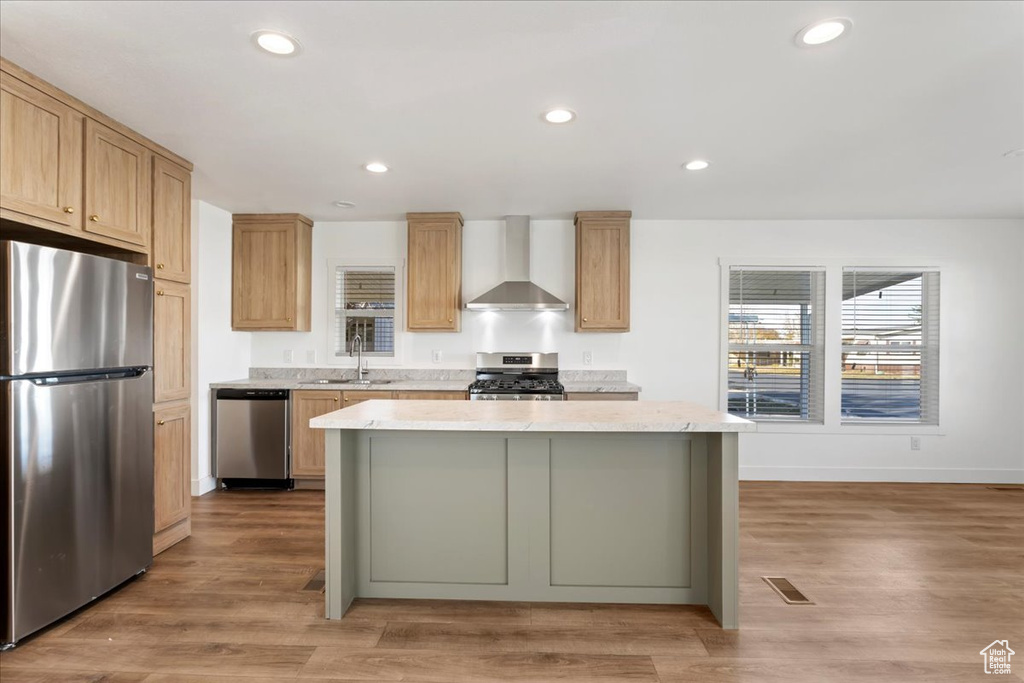 Kitchen with wall chimney range hood, appliances with stainless steel finishes, recessed lighting, baseboards, and a kitchen island