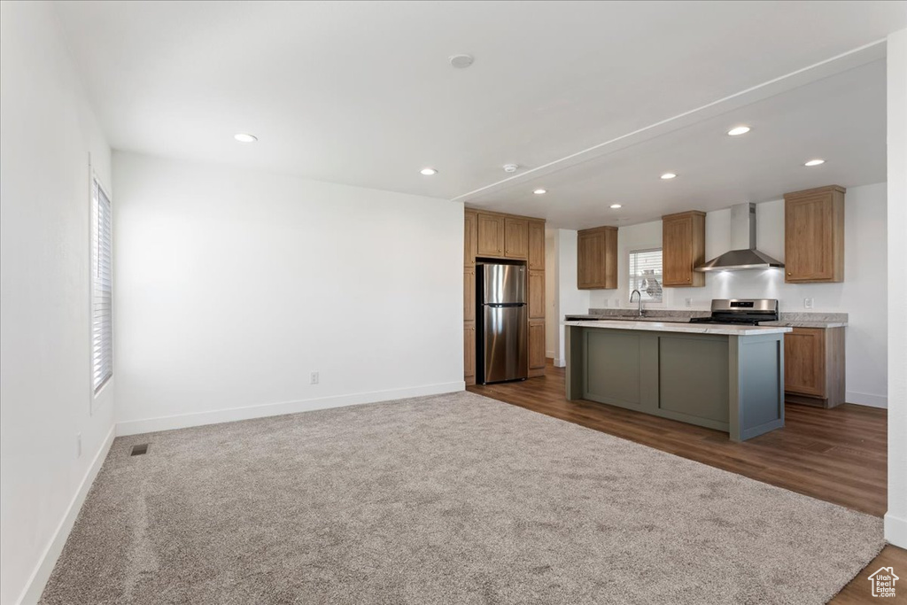 Kitchen featuring a kitchen island, appliances with stainless steel finishes, light countertops, baseboards, and wall chimney exhaust hood