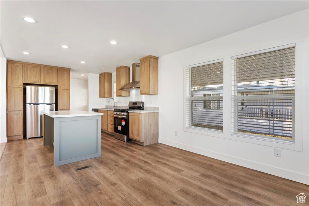 Kitchen with appliances with stainless steel finishes, light countertops, baseboards, light wood-style floors, and wall chimney exhaust hood