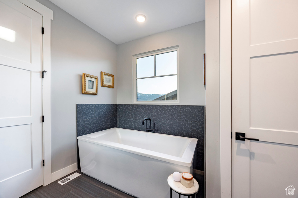 Bathroom with baseboards, a freestanding bath, wallpapered walls, and wood finished floors
