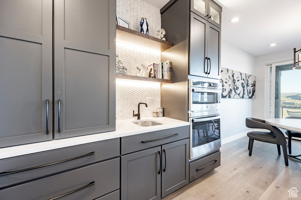 Kitchen with open shelves, decorative backsplash, double oven, a sink, and gray cabinetry