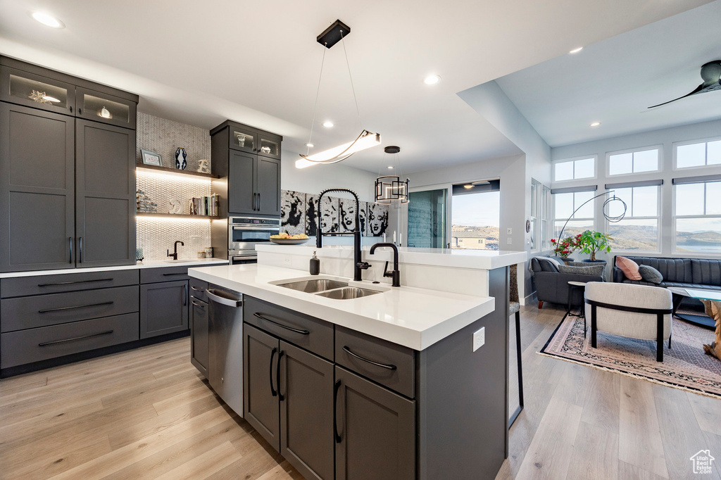 Kitchen with backsplash, light countertops, light wood-style floors, stainless steel appliances, and an island with sink