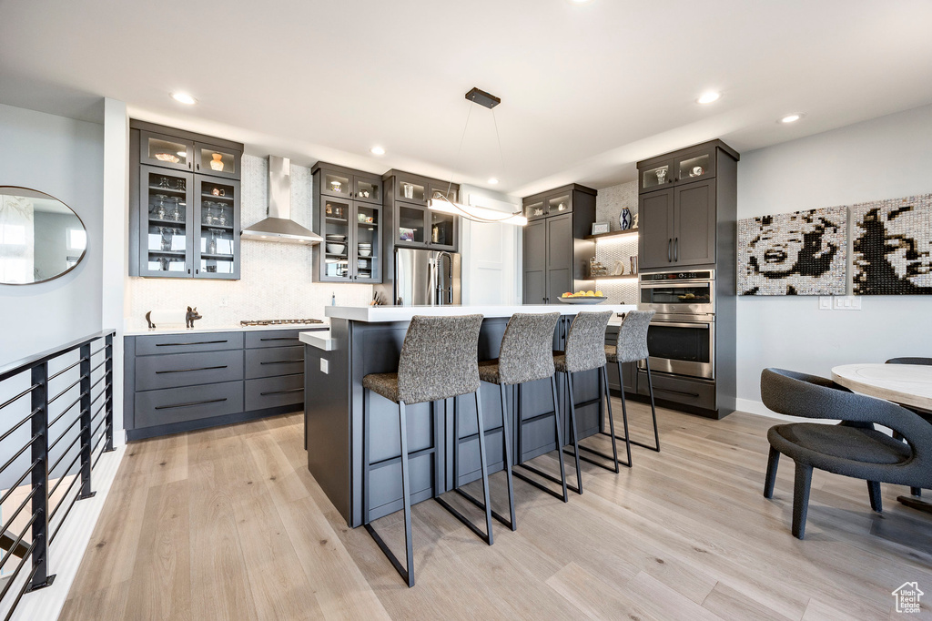 Kitchen with light countertops, wall chimney exhaust hood, appliances with stainless steel finishes, and backsplash