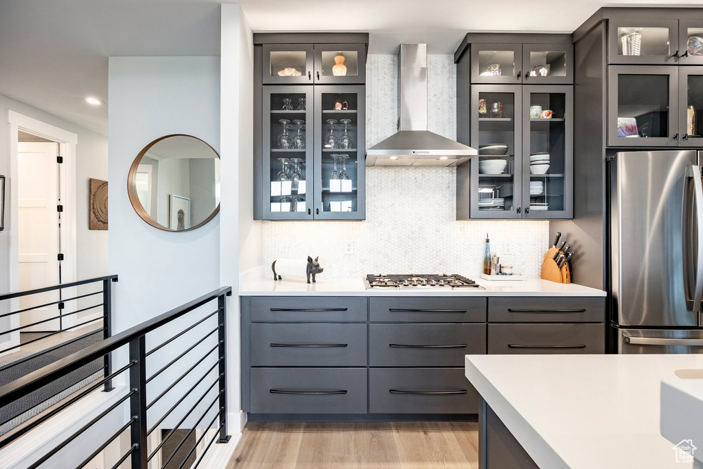 Kitchen with wall chimney exhaust hood, appliances with stainless steel finishes, backsplash, light countertops, and glass insert cabinets