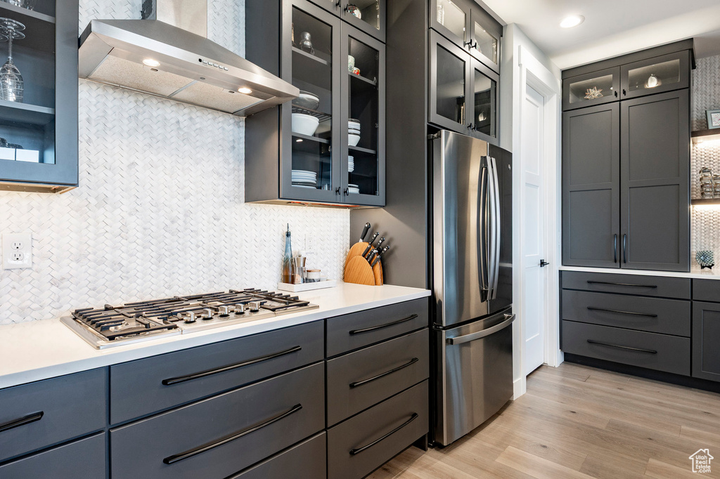 Kitchen featuring wall chimney exhaust hood, light wood finished floors, backsplash, and stainless steel appliances