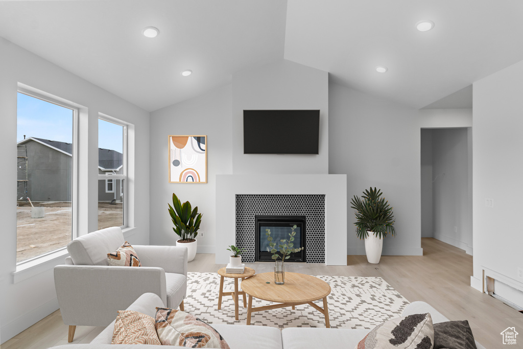 Living room featuring vaulted ceiling, light wood-type flooring, baseboards, a glass covered fireplace, and recessed lighting