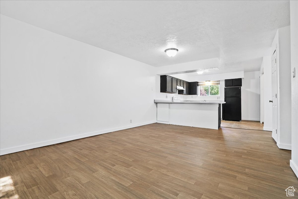 Unfurnished living room with baseboards, a textured ceiling, and light wood-style flooring