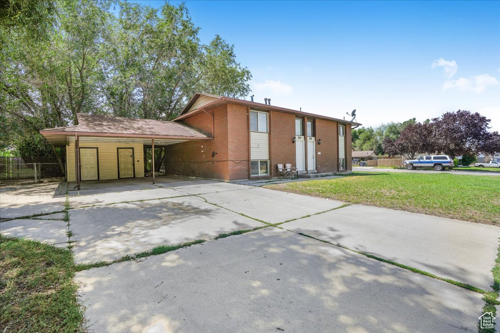 View of front of home featuring driveway, a front yard, brick siding, fence, and an attached carport