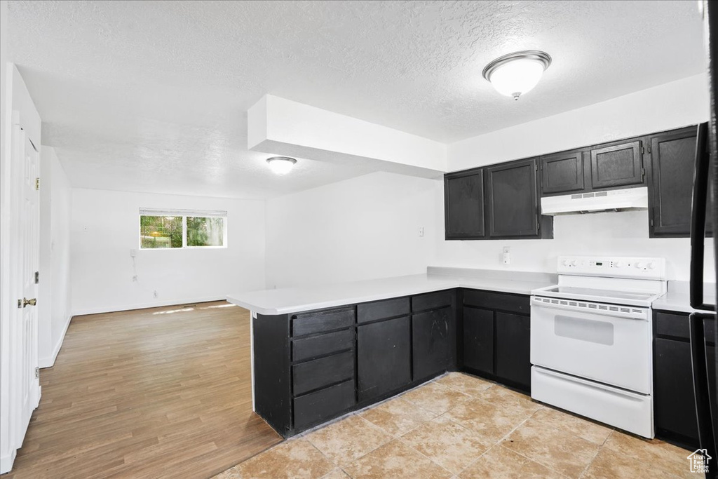 Kitchen with white electric range oven, dark cabinetry, light countertops, a peninsula, and under cabinet range hood
