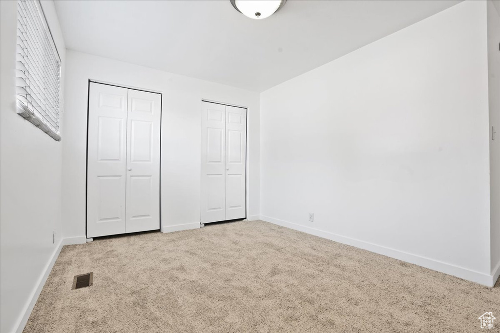 Unfurnished bedroom with baseboards, carpet, two closets, and visible vents