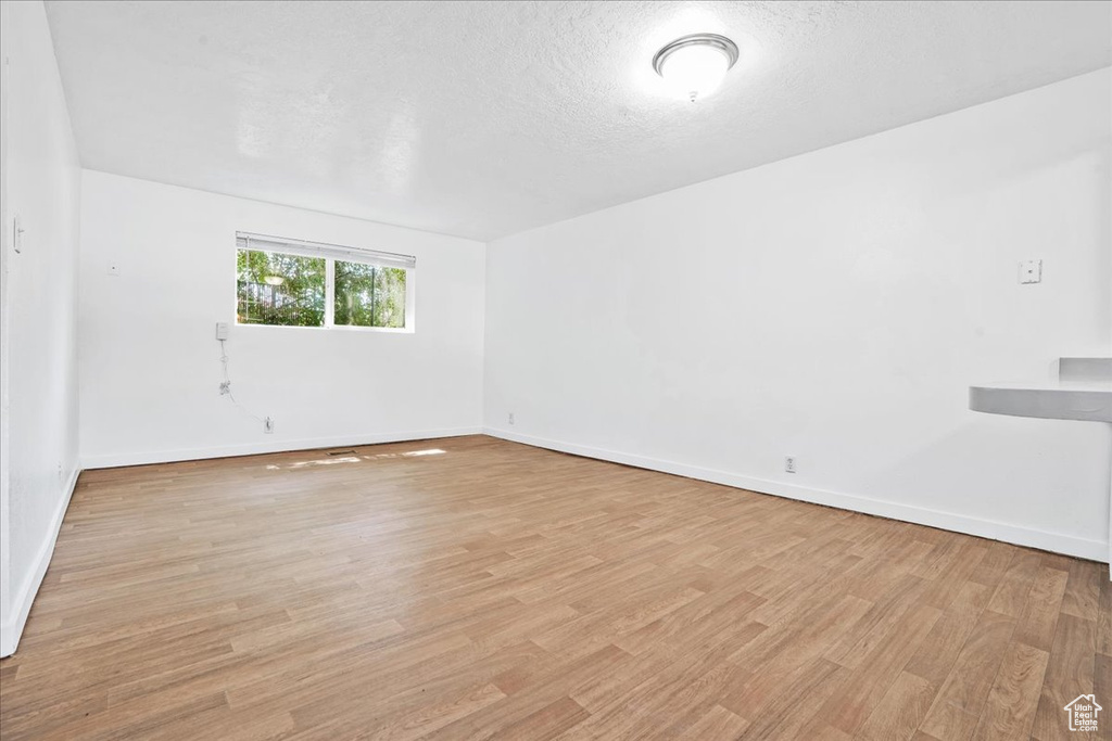 Unfurnished room with baseboards, a textured ceiling, and light wood-style flooring