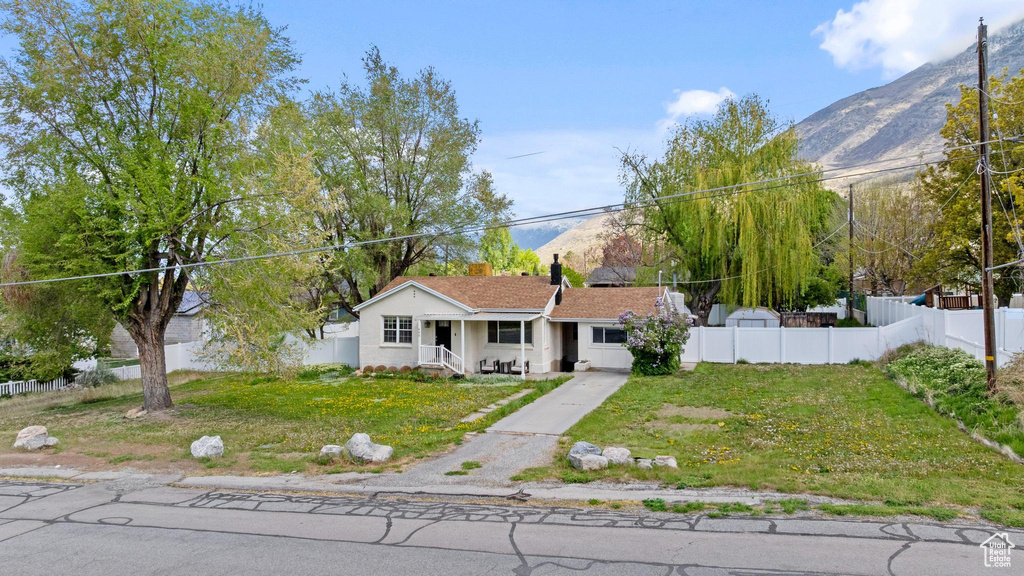 View of front of house featuring fence, a mountain view, a porch, and a front lawn