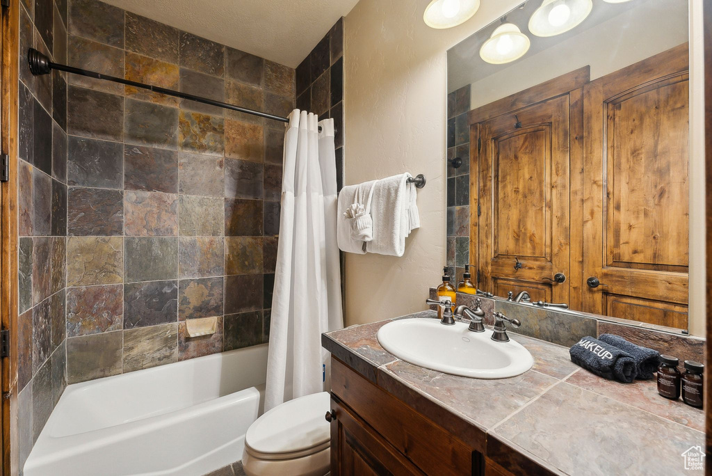 Bathroom with vanity, shower / bath combo, and toilet