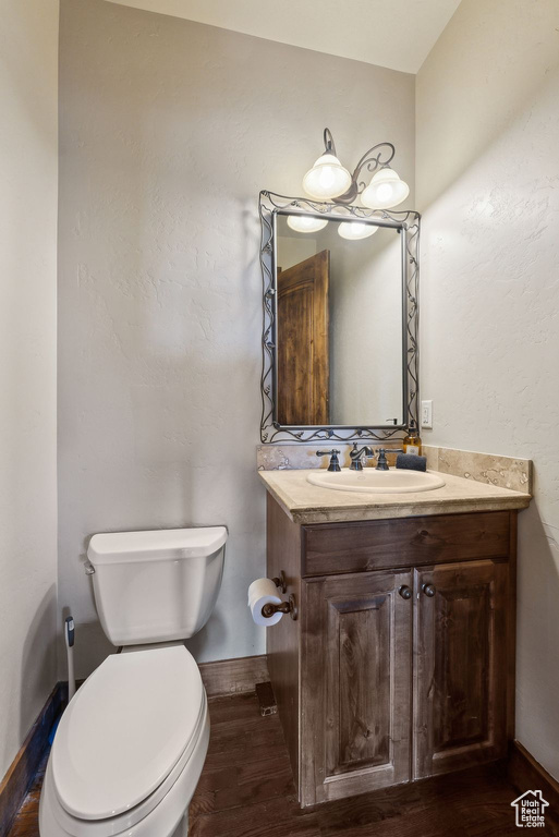 Half bathroom with vanity, baseboards, wood finished floors, and toilet
