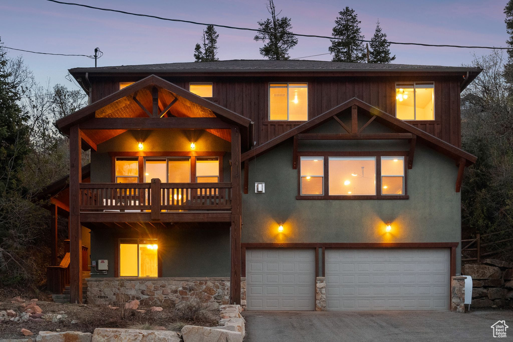 View of front of home with stone siding, a garage, stucco siding, concrete driveway, and a balcony