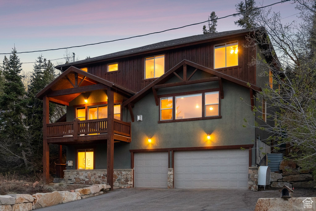 Rustic home featuring stone siding, a garage, aphalt driveway, stucco siding, and a balcony
