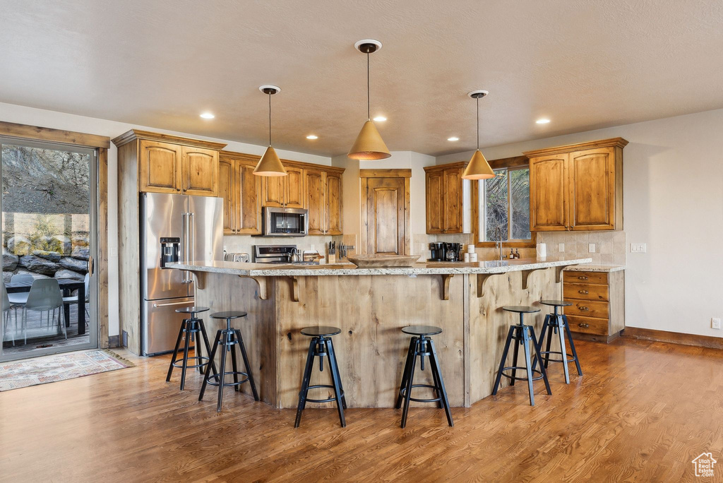 Kitchen featuring a breakfast bar area, stainless steel appliances, wood finished floors, and backsplash