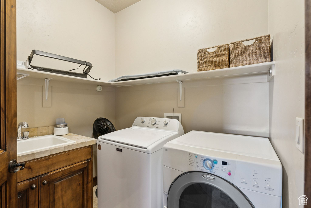 Clothes washing area featuring separate washer and dryer, a sink, and cabinet space