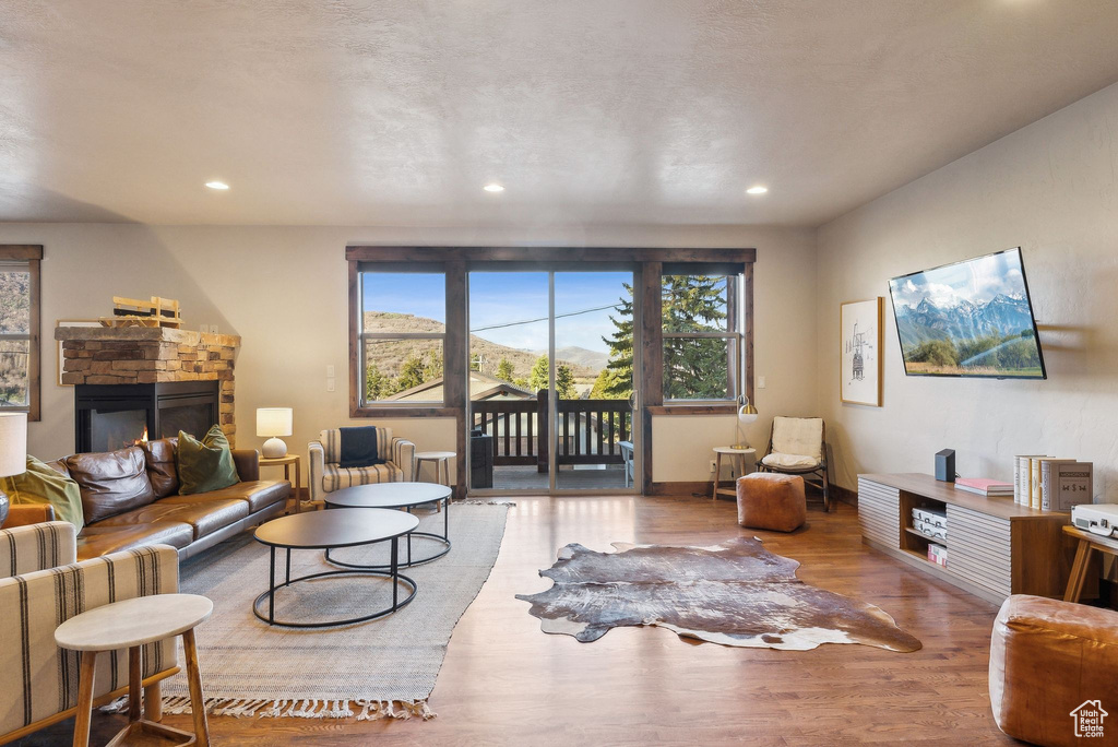 Living area with recessed lighting, a stone fireplace, a healthy amount of sunlight, and wood finished floors