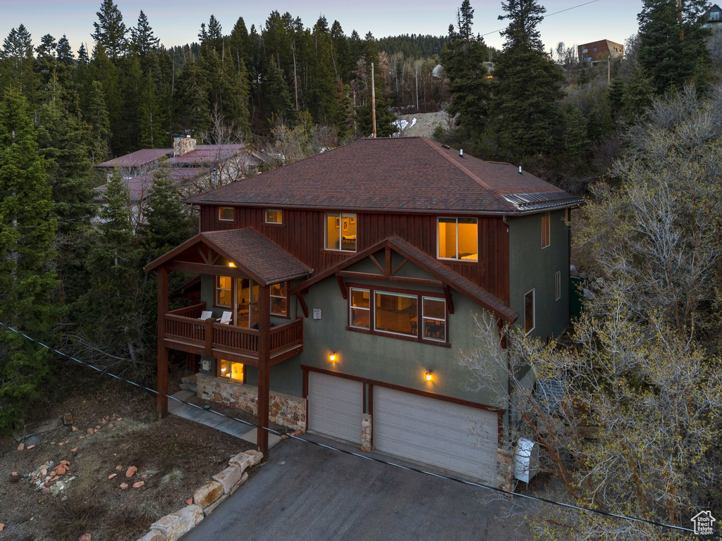 Rustic home featuring a forest view, roof with shingles, aphalt driveway, an attached garage, and stone siding