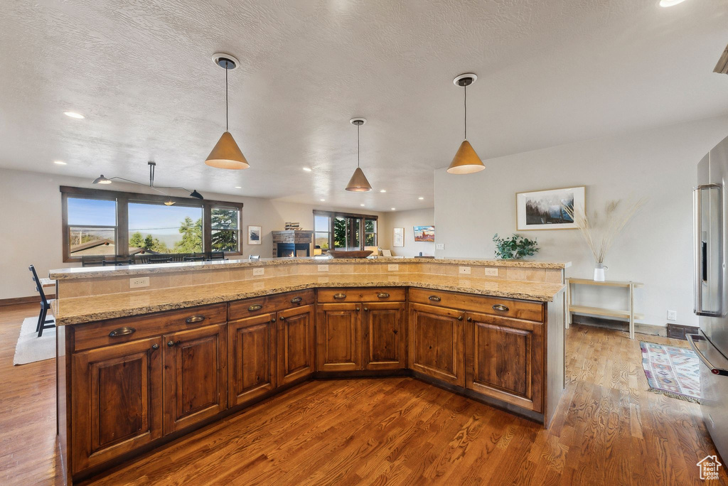 Kitchen with decorative light fixtures, brown cabinets, high quality fridge, light stone counters, and dark wood-type flooring